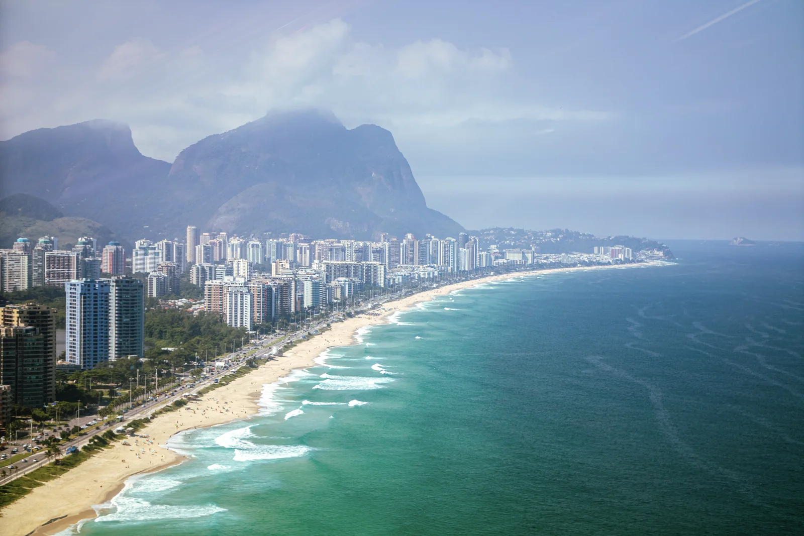 Barra da Tijuca's coastline seen from above between the city, ocean and mountains.