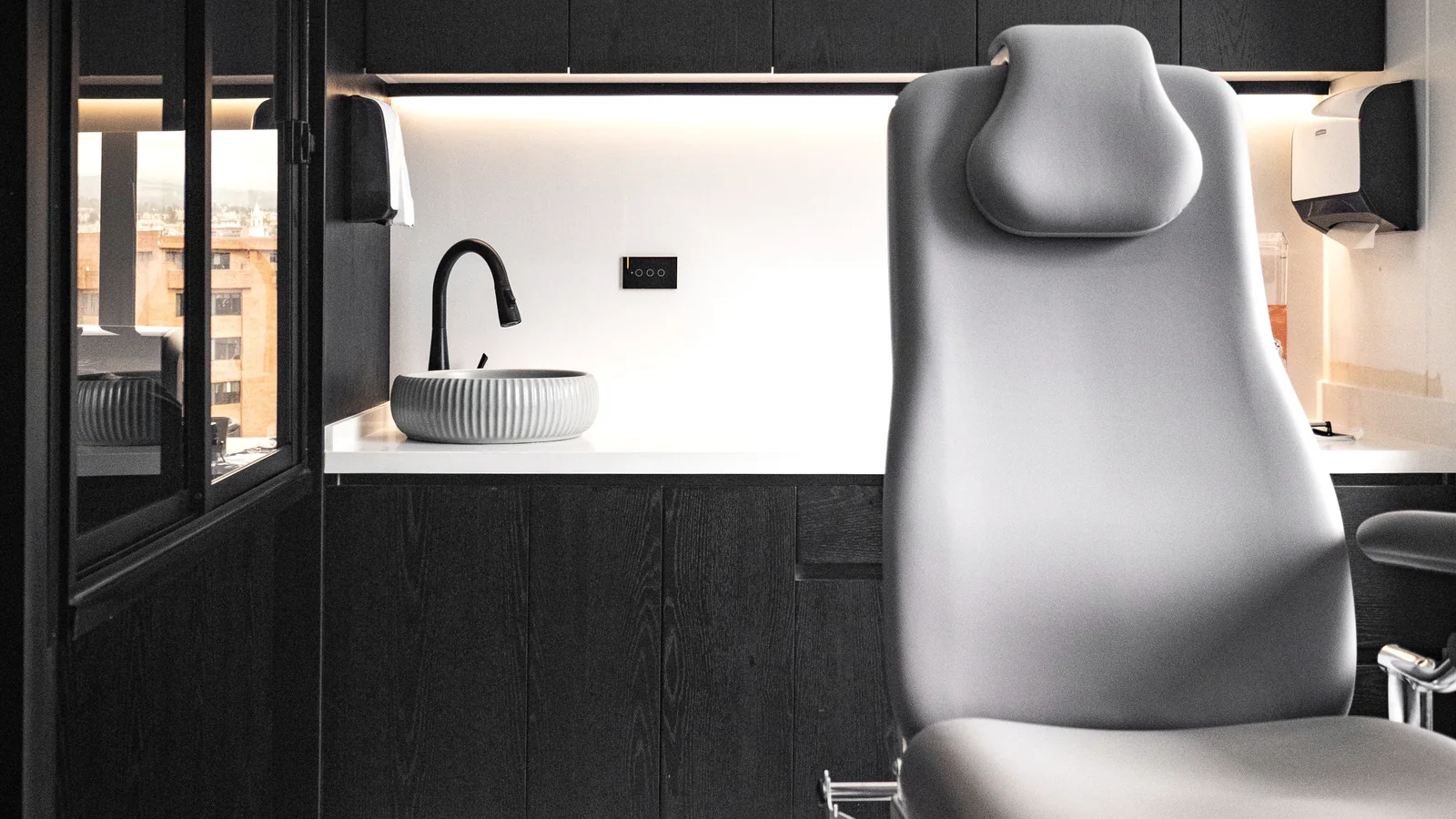 Contemporary dental treatment room with a clinical chair, dark cabinetry and indirect lighting.